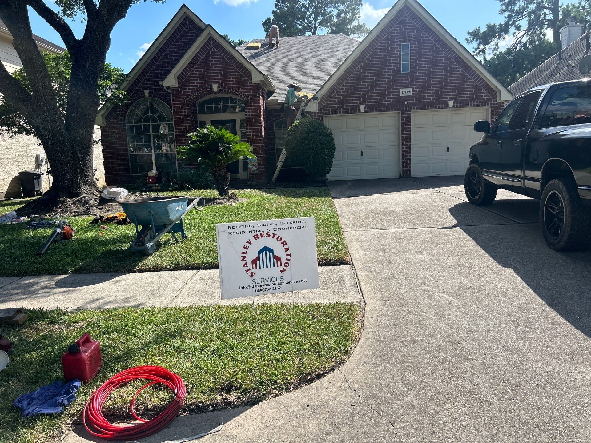 Stanley Restoration Services crew on a Houston brick home, ladder at the eave, yard sign in the grass